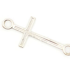 May include: Silver cross charm with two rings on either end. The cross has a textured design.