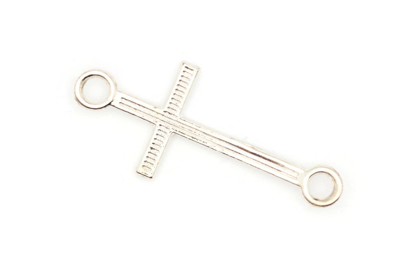 May include: Silver cross charm with two rings on either end. The cross has a textured design.