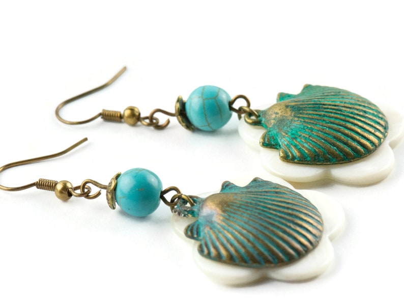 May include: A pair of turquoise and bronze earrings with a shell design. The earrings feature a turquoise bead and a bronze shell with a white flower-shaped base.