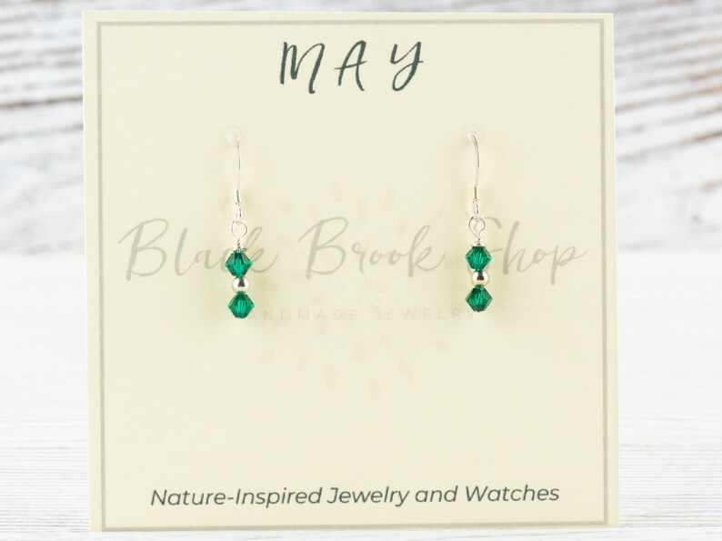 Peut inclure: Une paire de boucles d'oreilles en argent avec des perles de cristal vertes. Les boucles d'oreilles sont sur une carte blanche avec le mot "MAI" et le texte "Black Brook Shop Bijoux et montres inspir&eacute;s de la nature".