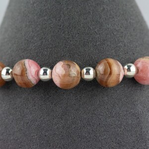 May include: A bracelet made with pink and brown patterned beads and silver spacer beads.