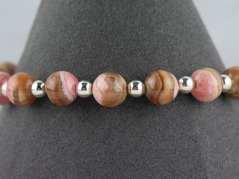 May include: A bracelet made with pink and brown patterned beads and silver spacer beads.