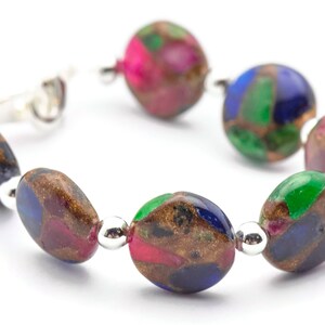 May include: A bracelet made of oval-shaped, multi-colored beads with silver accents. The beads are a mix of green, blue, pink, and brown.