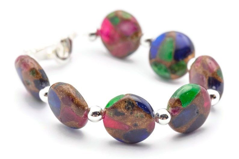 May include: A bracelet made of oval-shaped, multi-colored beads with silver accents. The beads are a mix of green, blue, pink, and brown.
