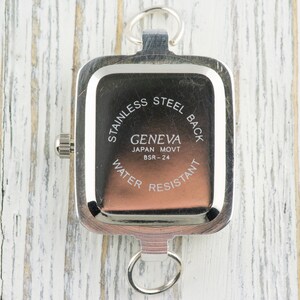 Pu&ograve; includere: Un orologio Geneva argentato con quadrante rettangolare e retro in acciaio inossidabile. L'orologio ha un piccolo quadrante e due anelli per il fissaggio. Il testo "GENEVA JAPAN MOVT BSR-24 WATER RESISTANT" &egrave; visibile.