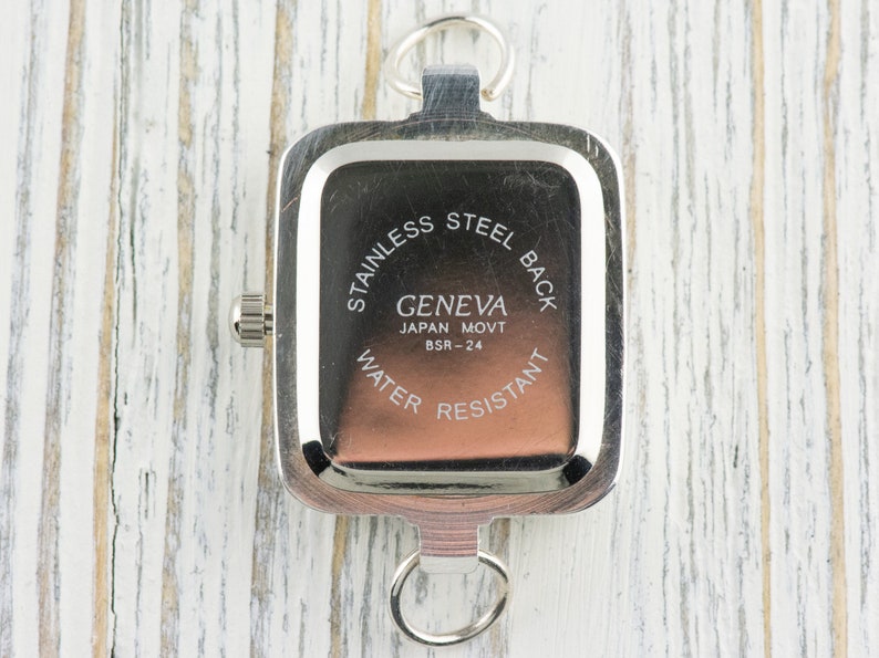 Pu&ograve; includere: Un orologio Geneva argentato con quadrante rettangolare e retro in acciaio inossidabile. L'orologio ha un piccolo quadrante e due anelli per il fissaggio. Il testo "GENEVA JAPAN MOVT BSR-24 WATER RESISTANT" &egrave; visibile.