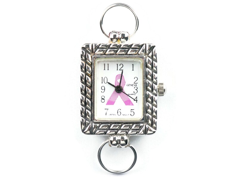 May include: A silver-toned rectangular pocket watch with a white face featuring black numerals and a pink ribbon. The watch has a textured frame and two circular attachments. The watch face reads "GENEVA QUARTZ".