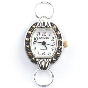 Peut inclure: Montre Geneva &agrave; quartz ovale avec un cadran blanc, des aiguilles noires et des accents dor&eacute;s. La montre a une lunette argent&eacute;e avec des clous noirs et dor&eacute;s. La montre est attach&eacute;e &agrave; un anneau argent&eacute; en haut et en bas.