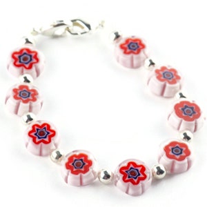 Puede incluir: Un brazalete de plata con cuentas de color rosa y blanco en forma de flor con centros rojos y azules.