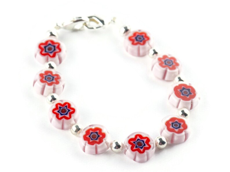 Puede incluir: Un brazalete de plata con cuentas de color rosa y blanco en forma de flor con centros rojos y azules.