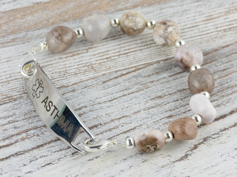 May include: A silver medical alert bracelet with a silver tag that reads "ASTHMA" and a medical symbol. The bracelet is made with brown and white agate beads.