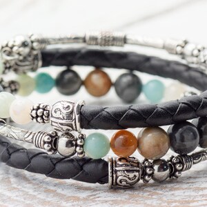 May include: A black leather bracelet with silver beads and a variety of semi-precious stones, including green, brown, and gray.