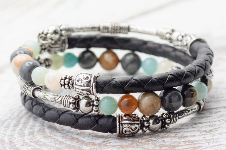 May include: A black leather bracelet with silver beads and a variety of semi-precious stones, including green, brown, and gray.