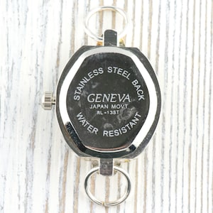 May include: A silver-toned Geneva watch with a stainless steel back and water-resistant design. The watch has a hexagonal shape and two key rings. The text "GENEVA JAPAN MOVT RL-13ST" is visible.
