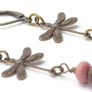 Puede incluir: Un par de pendientes colgantes con un dije de lib&eacute;lula y dos cuentas de color rosa y marr&oacute;n. Los dijes de lib&eacute;lula est&aacute;n hechos de metal y tienen un acabado bronce. Las cuentas est&aacute;n hechas de piedra y tienen un acabado natural.