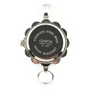 May include: A silver-toned Geneva watch with a floral-shaped bezel and two key rings. The watch back is black with white text that reads "STAINLESS STEEL BACK", "GENEVA JAPAN MOVT RL-255T", and "WATER RESISTANT".