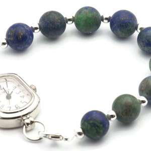 May include: A silver watch with a square face and a beaded bracelet made of blue and green stones.