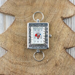 May include: A silver pocket watch with a white face and a Santa Claus design. The watch has a decorative border and is attached to a silver chain.