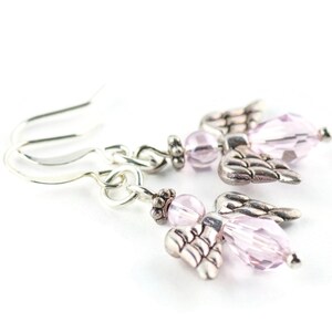 May include: A pair of silver angel wing earrings with pink crystal beads. The earrings are dangle style and have a hook closure.