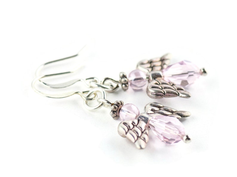 May include: A pair of silver angel wing earrings with pink crystal beads. The earrings are dangle style and have a hook closure.