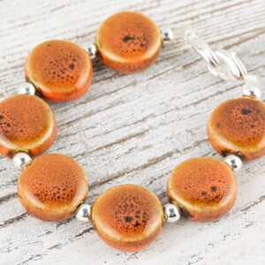 May include: A bracelet made of orange ceramic beads with a silver clasp. The beads have a speckled pattern.