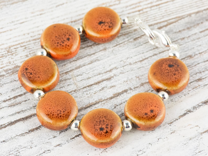 May include: A bracelet made of orange ceramic beads with a silver clasp. The beads have a speckled pattern.