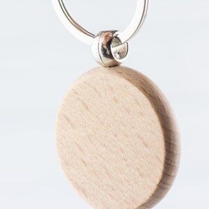Op de afbeelding: Een ronde, houten sleutelhanger met een zilveren ring. De sleutelhanger is leeg en kan worden gepersonaliseerd.