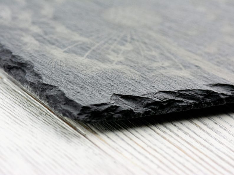 K&ouml;nnte beinhalten: Nahaufnahme einer schwarzen Schiefer-Servierplatte mit einer rauen, strukturierten Oberfl&auml;che. Die Platte ist angewinkelt und die Kanten sind leicht abgebrochen.