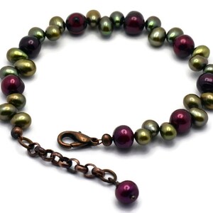 May include: A bracelet made of green and burgundy pearls with a copper clasp and extender chain.