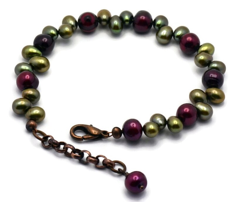 May include: A bracelet made of green and burgundy pearls with a copper clasp and extender chain.