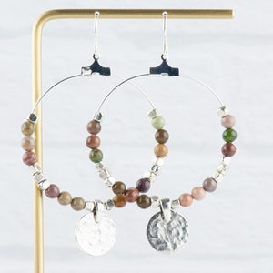 May include: Silver hoop earrings with a hammered silver charm and a beaded fringe of brown, green, and pink stones.