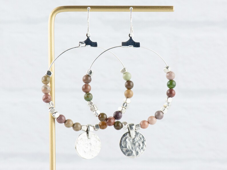 May include: Silver hoop earrings with a hammered silver charm and a beaded fringe of brown, green, and pink stones.