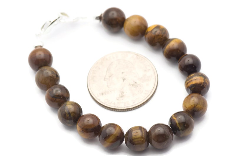 Op de afbeelding: Een bruine en gouden tijgeroog kralen armband met een zilveren sluiting. De armband ligt naast een Amerikaanse kwart voor referentie van de grootte.