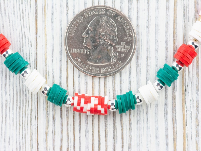 K&ouml;nnte beinhalten: Nahaufnahme eines Armbands aus wei&szlig;en, gr&uuml;nen und roten Perlen. Das Armband liegt auf einer wei&szlig;en Holzoberfl&auml;che mit einer US-amerikanischen 25-Cent-M&uuml;nze als Gr&ouml;&szlig;envergleich.