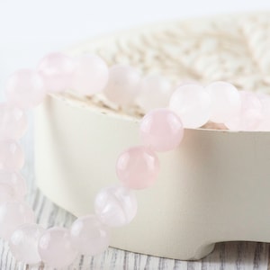 May include: A pink rose quartz bracelet with round beads. The bracelet is on a white background.