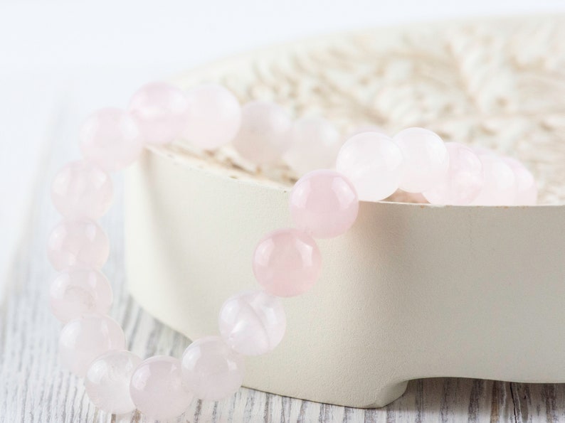 May include: A pink rose quartz bracelet with round beads. The bracelet is on a white background.