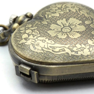 Puede incluir: Reloj de bolsillo antiguo en forma de coraz&oacute;n con grabados florales. El reloj tiene un acabado bronce y una cadena. La esfera del reloj est&aacute; decorada con un motivo floral. El reloj est&aacute; cerrado y tiene un cierre.