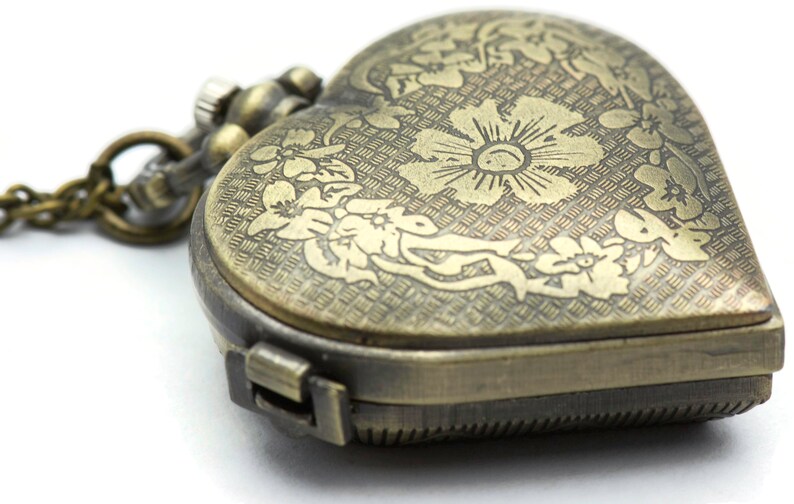 Puede incluir: Reloj de bolsillo antiguo en forma de coraz&oacute;n con grabados florales. El reloj tiene un acabado bronce y una cadena. La esfera del reloj est&aacute; decorada con un motivo floral. El reloj est&aacute; cerrado y tiene un cierre.