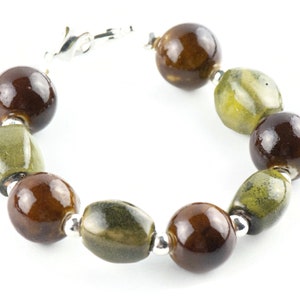 May include: A bracelet made of brown and green ceramic beads with silver accents.