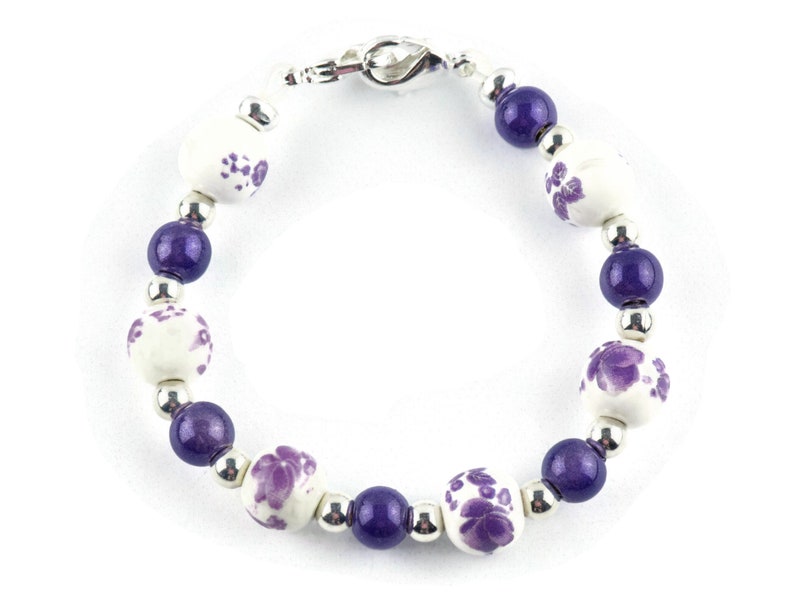 May include: A purple and white beaded bracelet with a silver clasp. The beads are round and have a floral design.