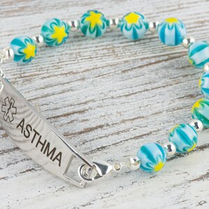 Peut inclure: Un bracelet d'alerte m&eacute;dicale en argent avec une cha&icirc;ne de perles &agrave; motifs bleus et jaunes. Le bracelet comporte une &eacute;tiquette indiquant "ASTHMA" avec un symbole m&eacute;dical.