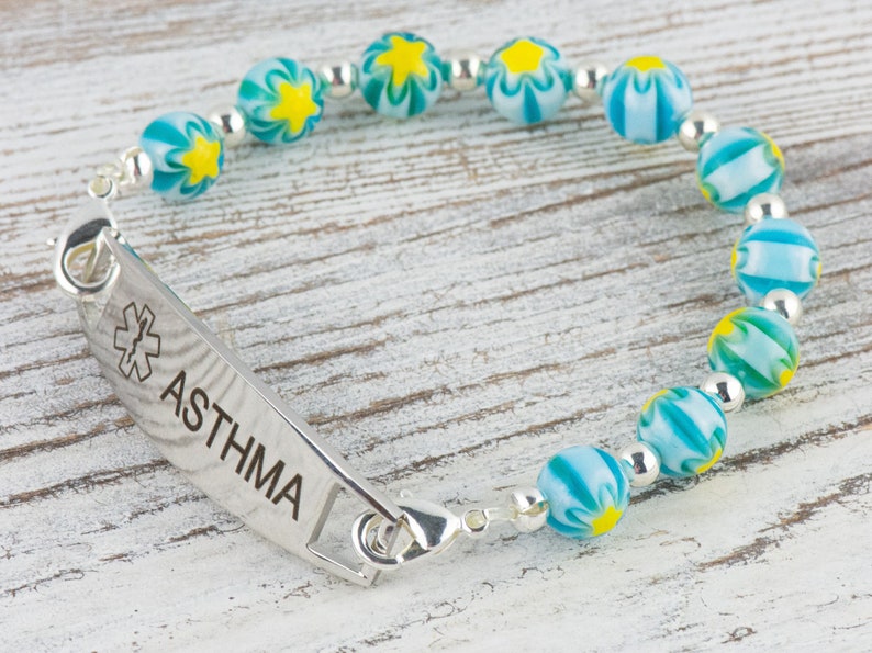 Peut inclure: Un bracelet d'alerte m&eacute;dicale en argent avec une cha&icirc;ne de perles &agrave; motifs bleus et jaunes. Le bracelet comporte une &eacute;tiquette indiquant "ASTHMA" avec un symbole m&eacute;dical.