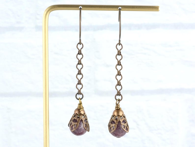 May include: A pair of drop earrings with a vintage style. Each earring has a small, round, purple gemstone in a filigree teardrop setting. The earrings hang from a chain of heart-shaped links.