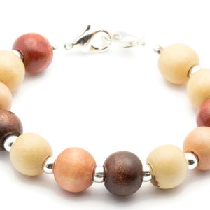 Puede incluir: Un brazalete de cuentas de madera con cuentas alternas de color marr&oacute;n claro, marr&oacute;n oscuro y marr&oacute;n rojizo. El brazalete tiene un cierre plateado.