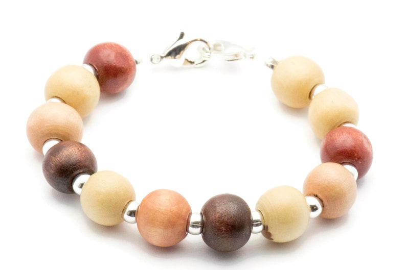 Puede incluir: Un brazalete de cuentas de madera con cuentas alternas de color marr&oacute;n claro, marr&oacute;n oscuro y marr&oacute;n rojizo. El brazalete tiene un cierre plateado.