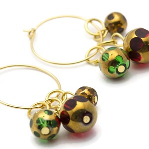 May include: Gold hoop earrings with dangling charms. The charms are round and have a gold base with green and red accents.