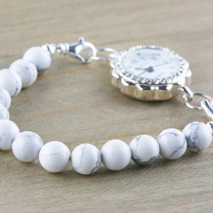 Peut inclure: Un bracelet de montre blanc et argent avec un cadran blanc et des aiguilles argent&eacute;es. Le bracelet est compos&eacute; de perles blanches et d'une cha&icirc;ne argent&eacute;e.