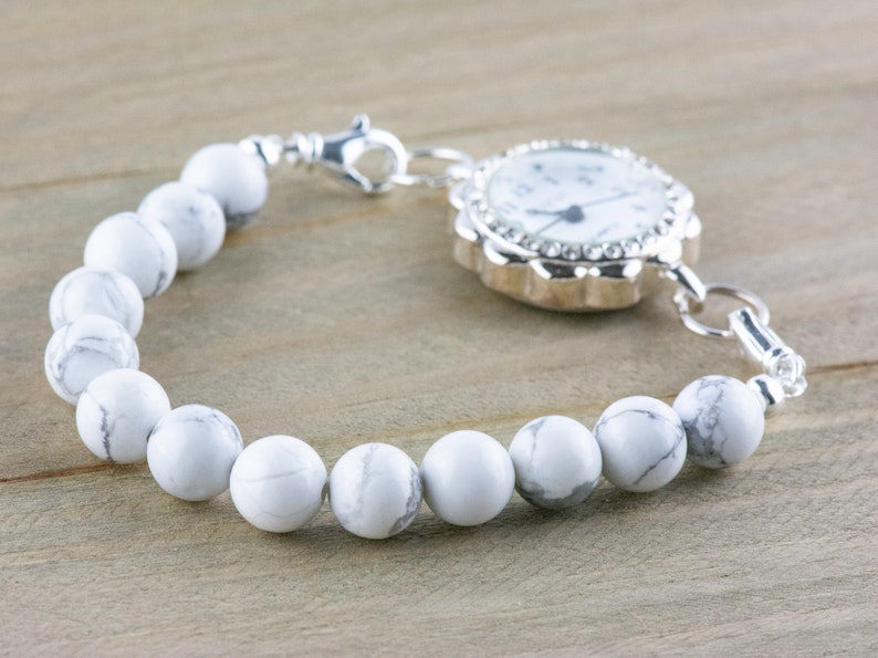 Peut inclure: Un bracelet de montre blanc et argent avec un cadran blanc et des aiguilles argent&eacute;es. Le bracelet est compos&eacute; de perles blanches et d'une cha&icirc;ne argent&eacute;e.
