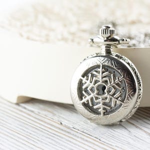 May include: A silver pocket watch with a snowflake design on the face.