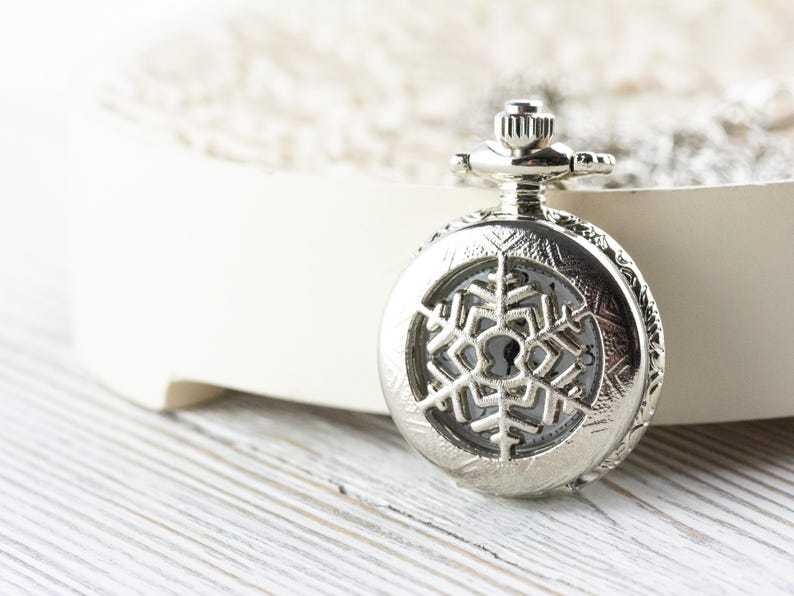 May include: A silver pocket watch with a snowflake design on the face.